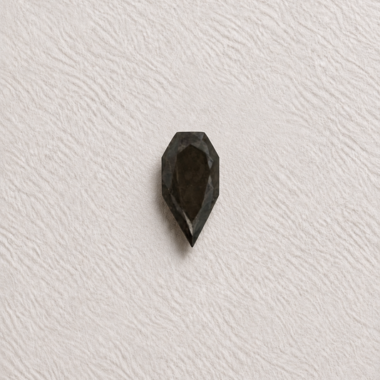 A single faceted dark gray gemstone with a teardrop or pear-like shape, centered on a textured off-white background.